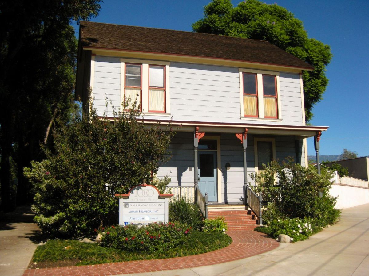 Light blue, two story home with a covered porch with shrubbery and a red brick pathway