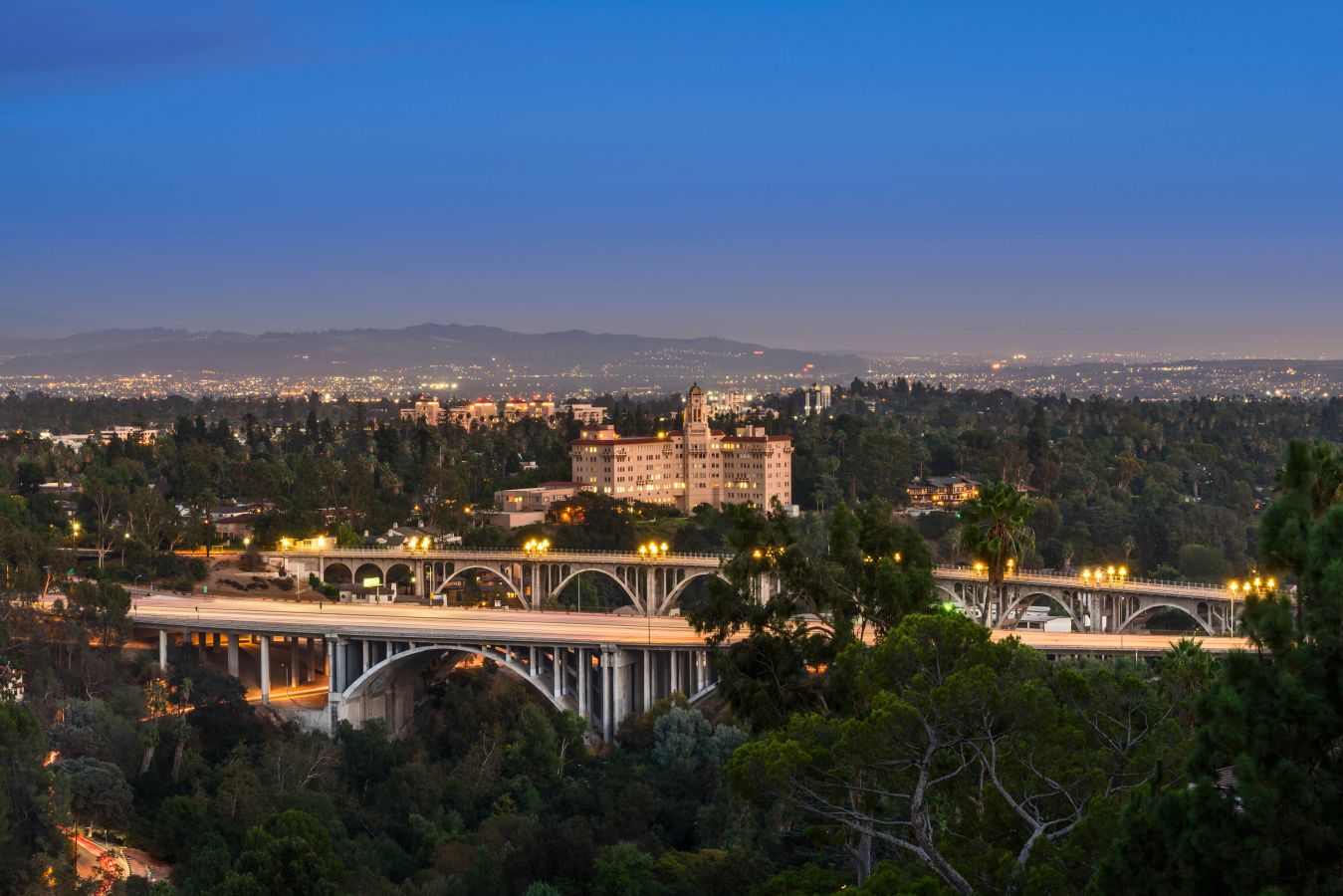 The Pasadena skyline at dusk with bridges, homes, and mountains in the distance