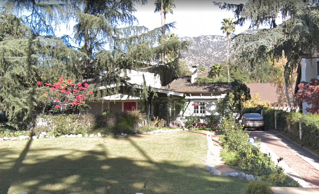 a home surrounded by trees and shrubbery. mountains can be seen between trees